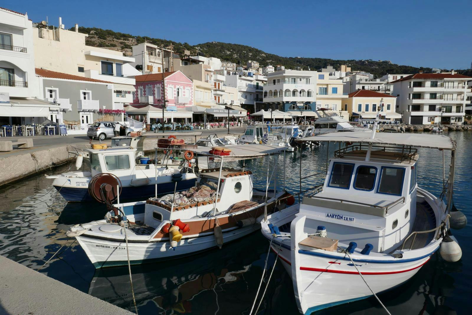 En lille havn med fiskerbåde og lystbåde med hvide huse i baggrunden.