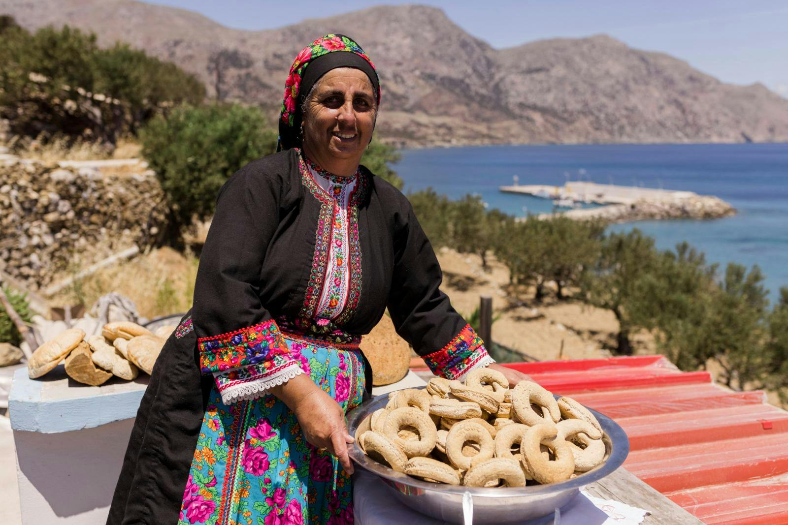 En kvinde klædt i traditionel, græsk kjole med en stor skål med brød. 