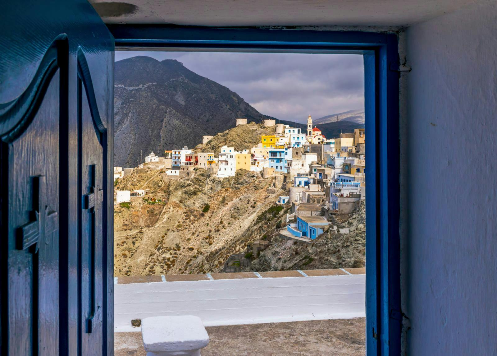 Udsigt fra vindue til bjerg med huse på. 