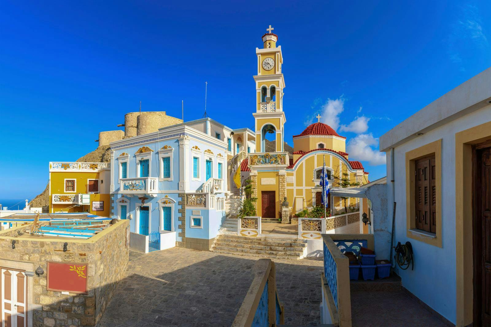 En kirkebygning med sandfarvet med hvide og blå huse i forgrunden. 