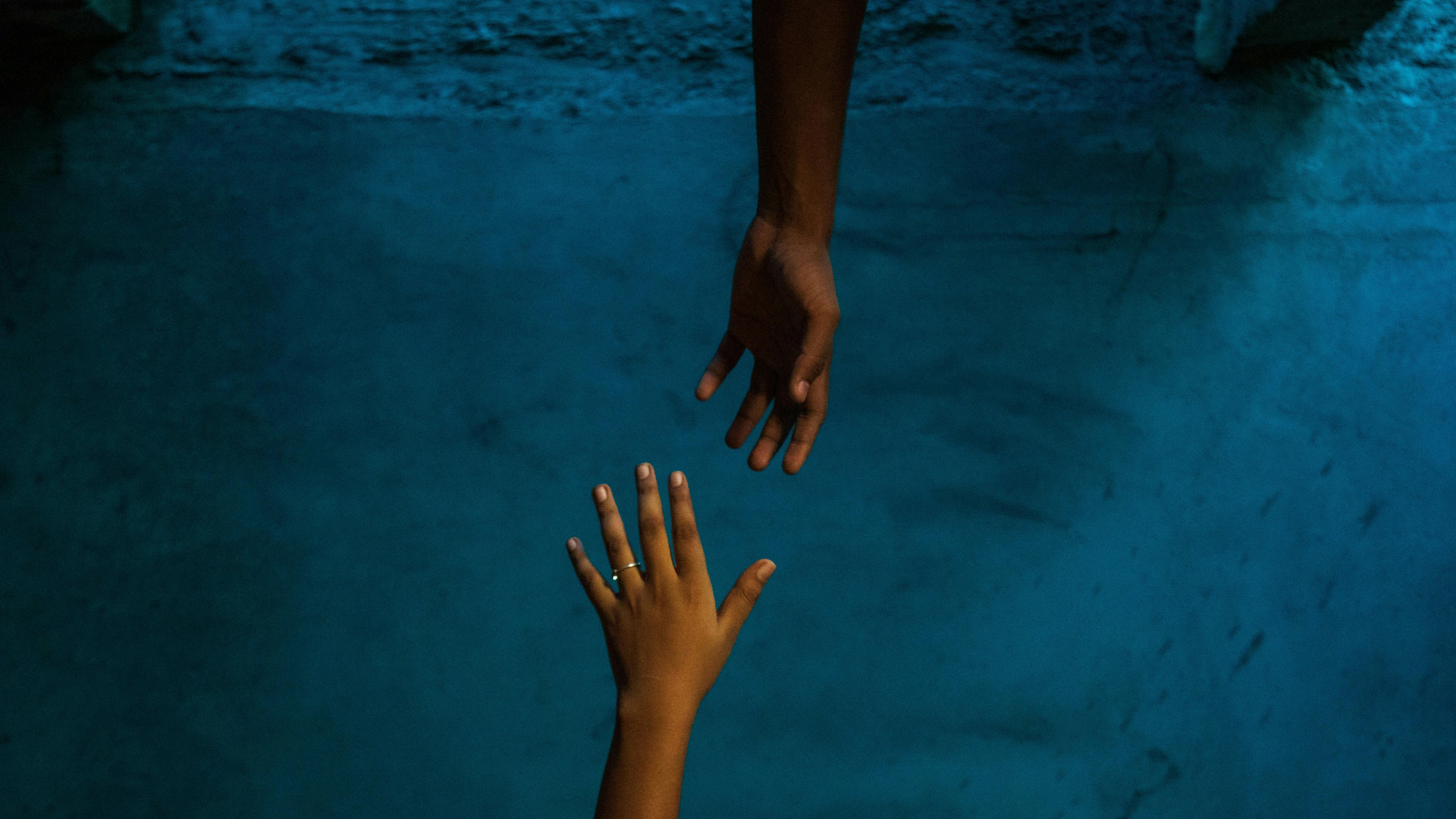 En hånd, der rækker ned i dybt vand for at gribe en anden hånd, der er ved at forsvinde i dybet.