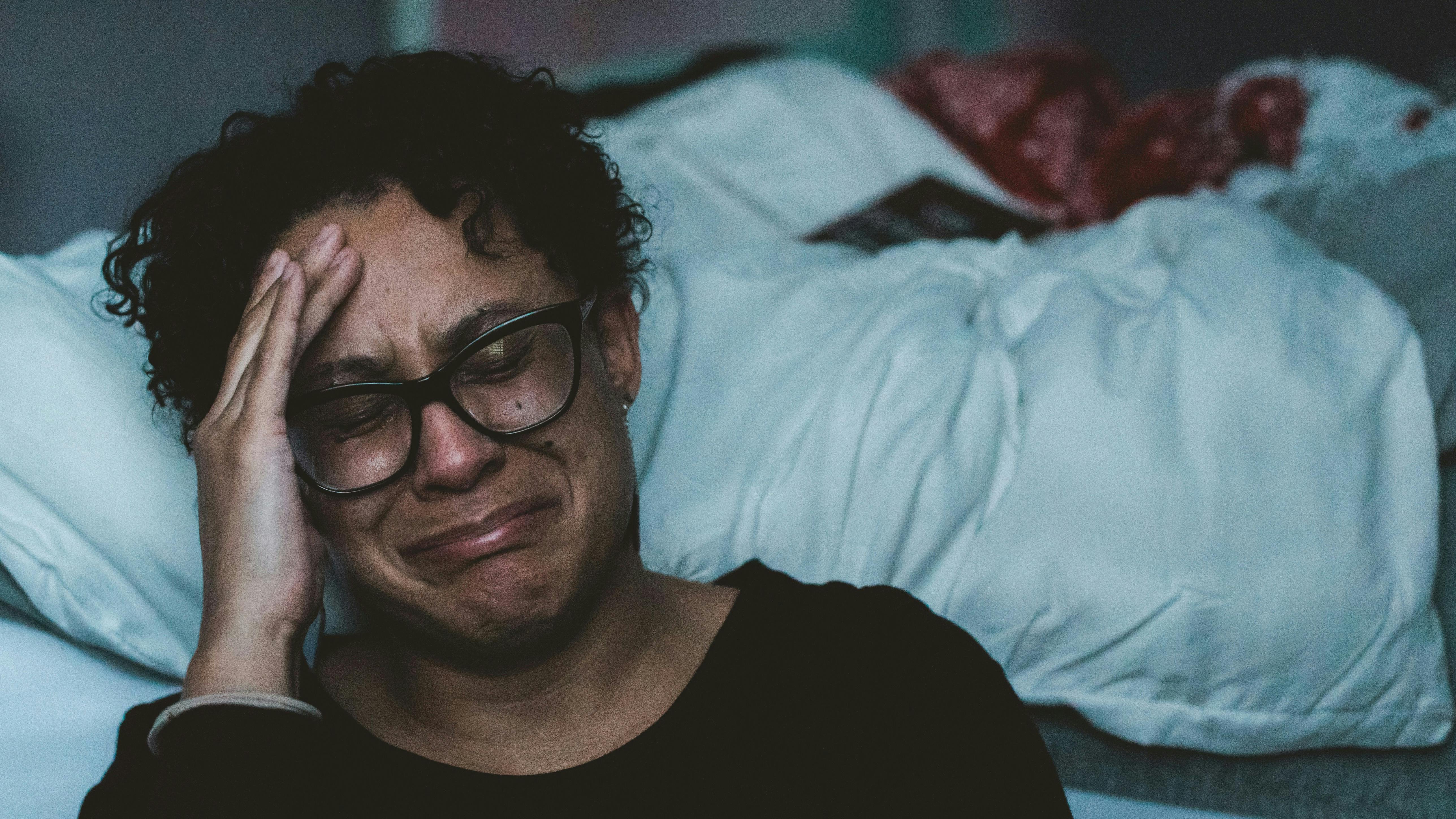 En kvinde, som sidder foran en seng og er ved at bryde sammen i gråd.