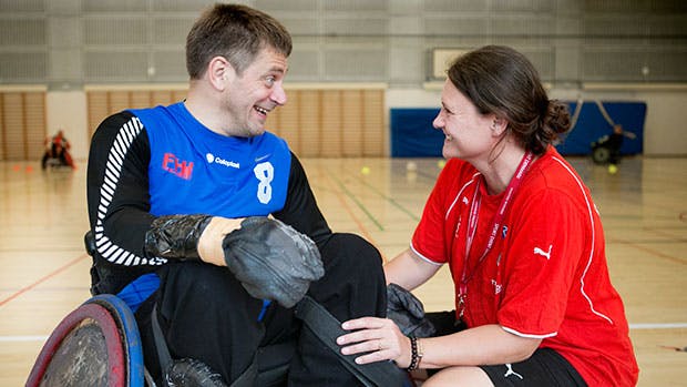 Mand sidder i en kørestol og dame sidder på hug ved siden af ham