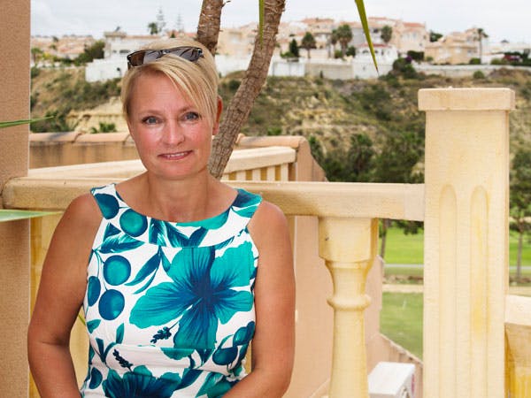 Leddegigt: Kvinde sidder på terrasse med palme i baggrund  