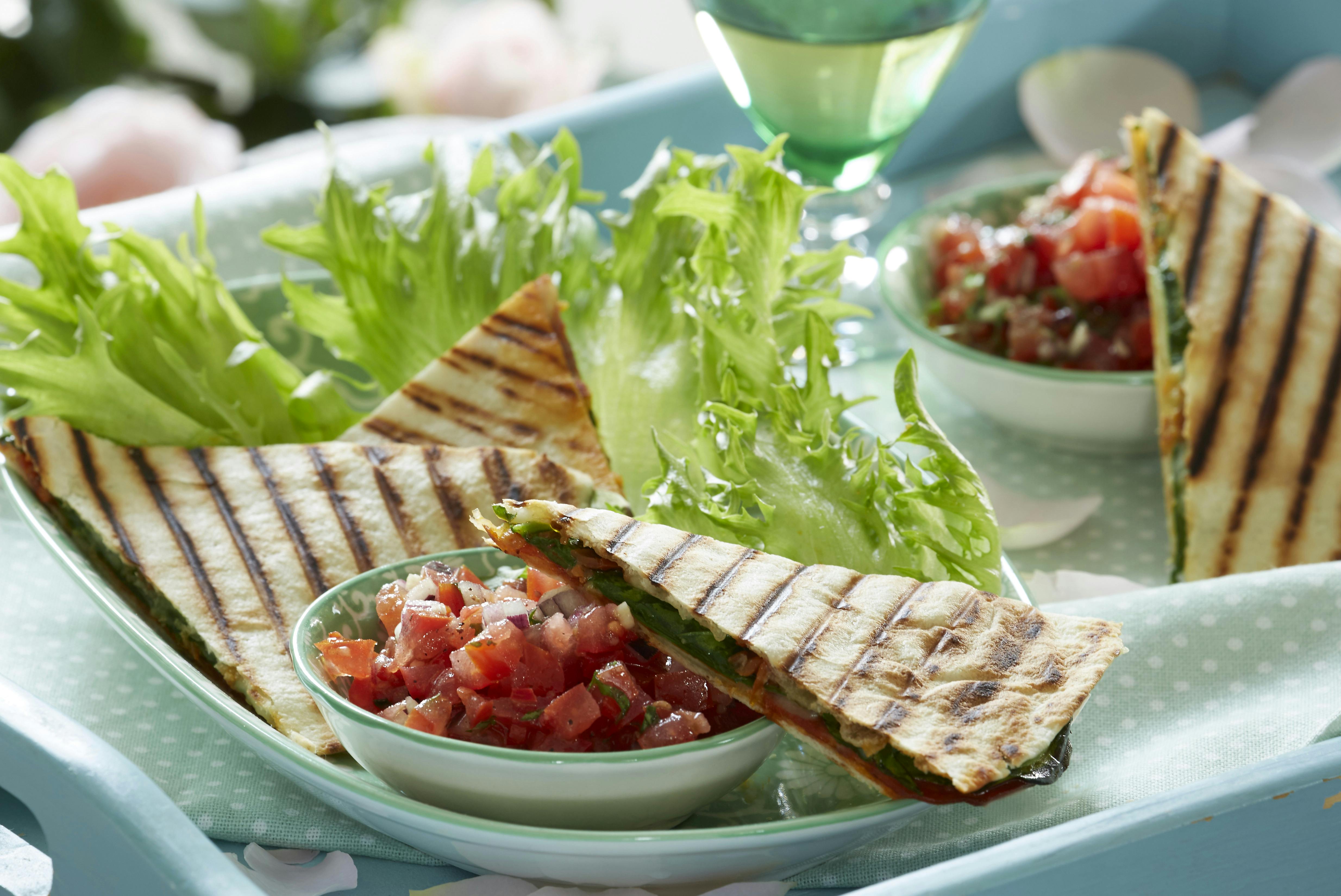 Quesadilla med fyld af spinat og mozzarella arrangeret på salatblade og ledsaget af en skål med tomatsalsa
