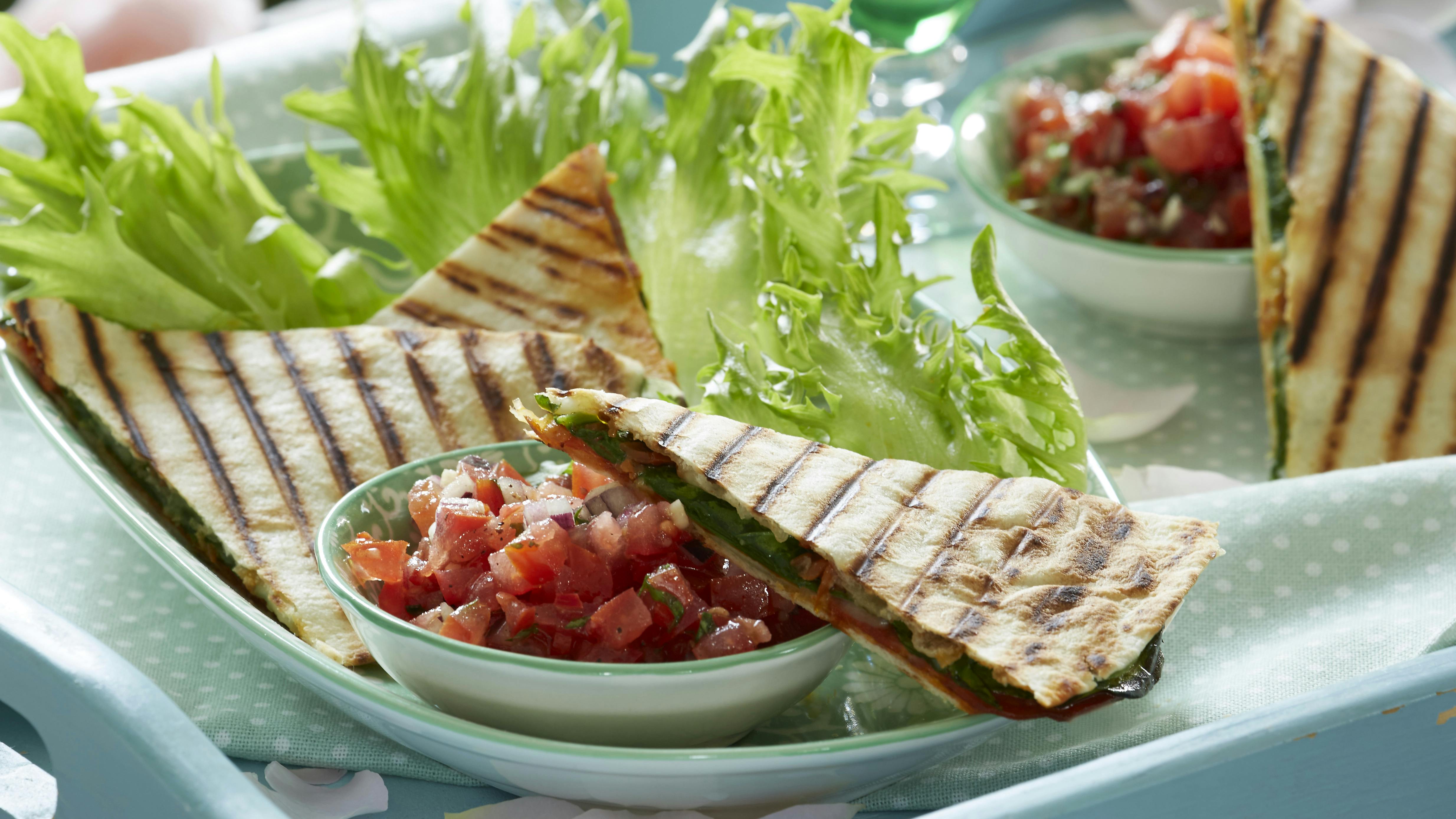 Quesadilla med fyld af spinat og mozzarella arrangeret på salatblade og ledsaget af en skål med tomatsalsa