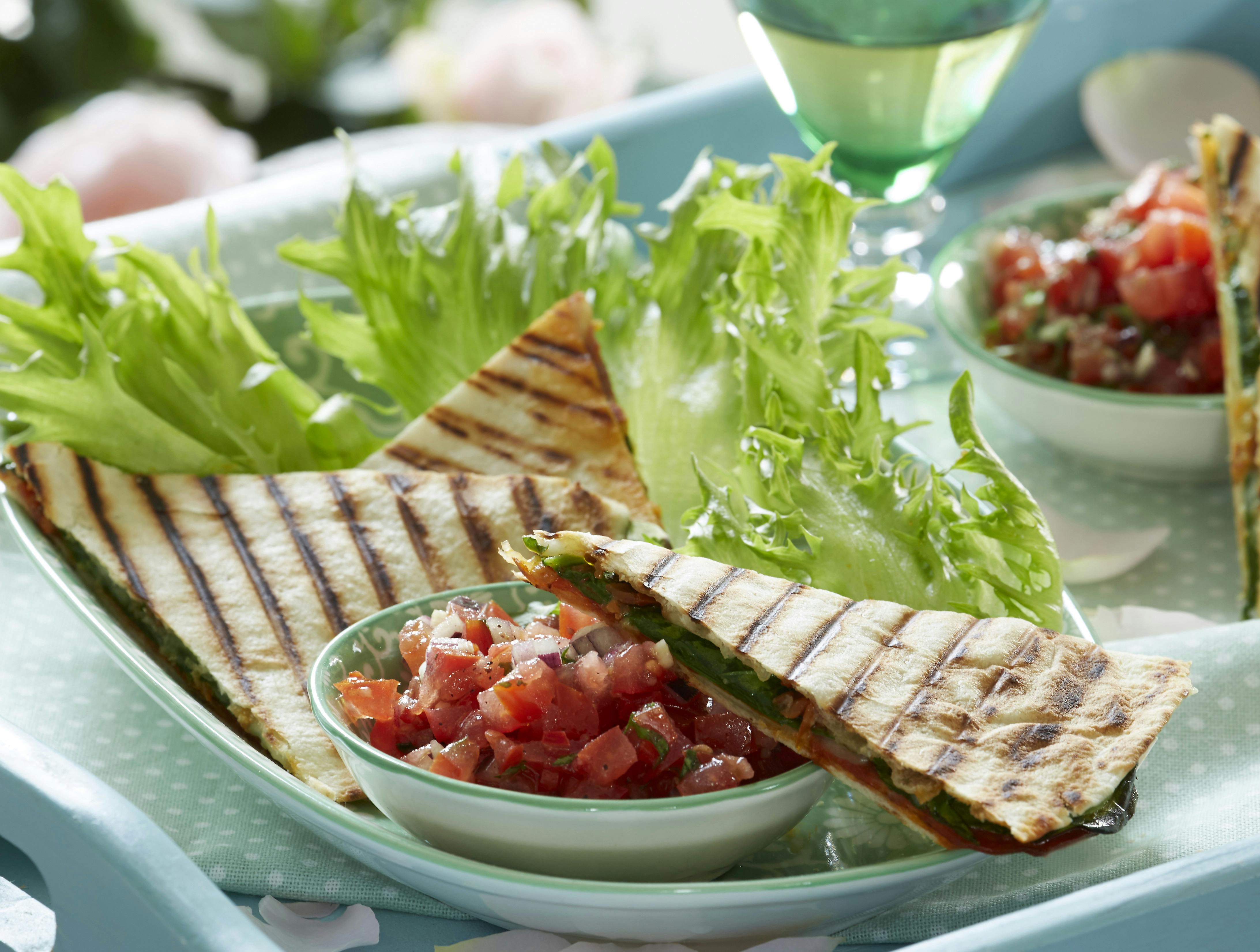 Quesadilla med fyld af spinat og mozzarella arrangeret på salatblade og ledsaget af en skål med tomatsalsa