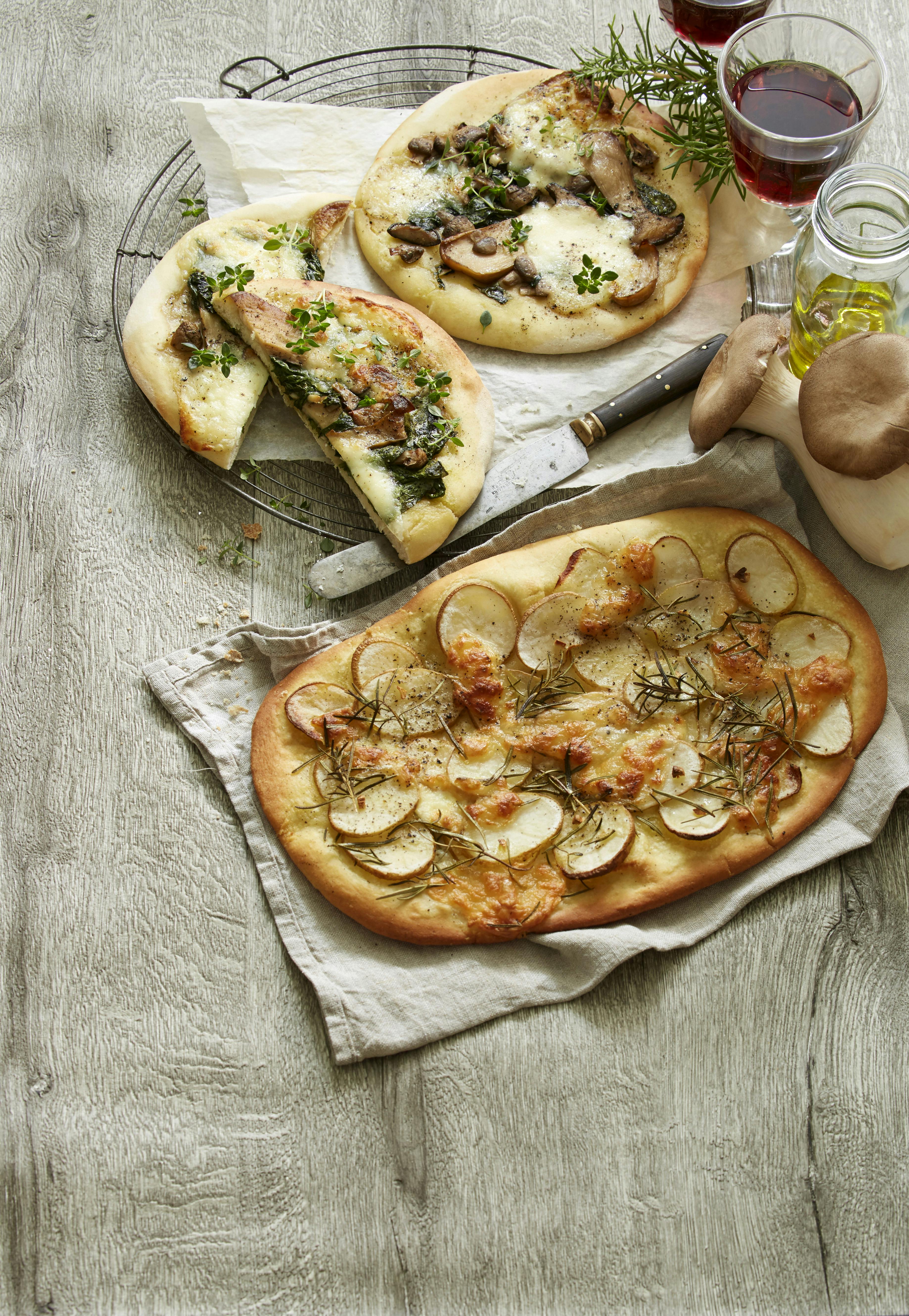 Oval pizza med fyld af tynde kartoffelskiver og herover mozzarella. På toppen kviste af rosmarin