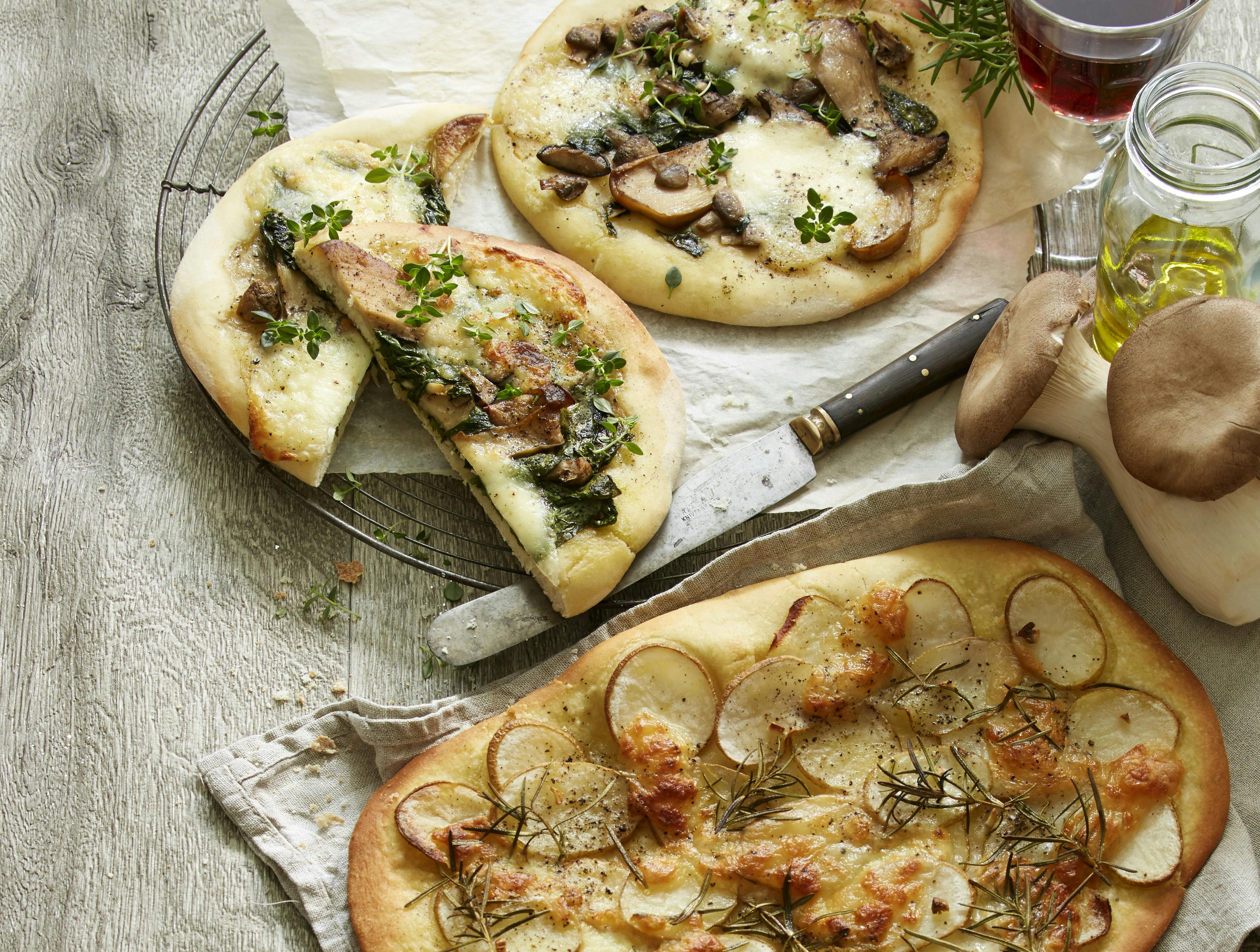 Oval pizza med fyld af tynde kartoffelskiver og herover mozzarella. På toppen kviste af rosmarin