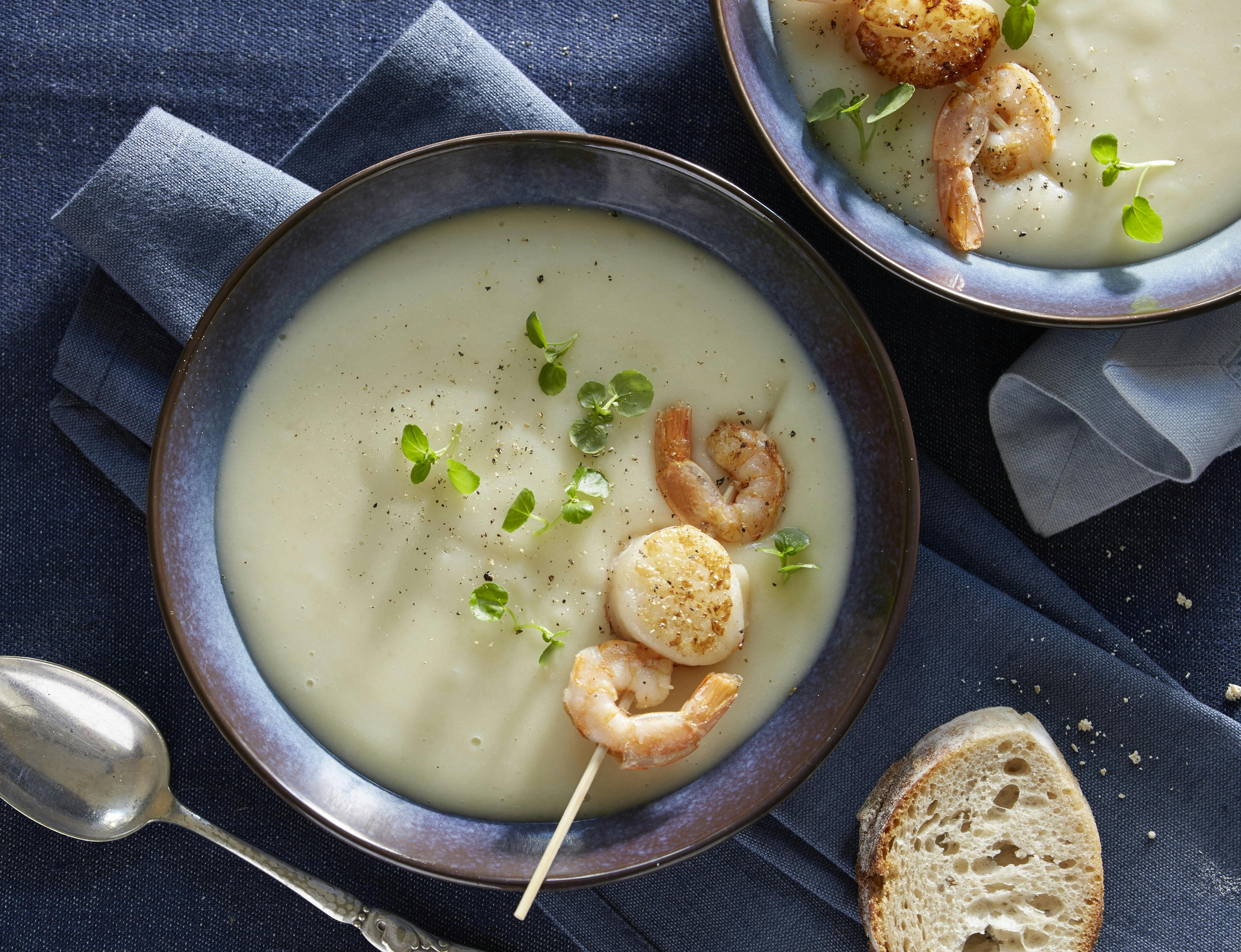 Cremet jordskoksuppe serveret med spyd med kæmperejer og små kammuslinger. Suppen er pyntet med brøndkarse.