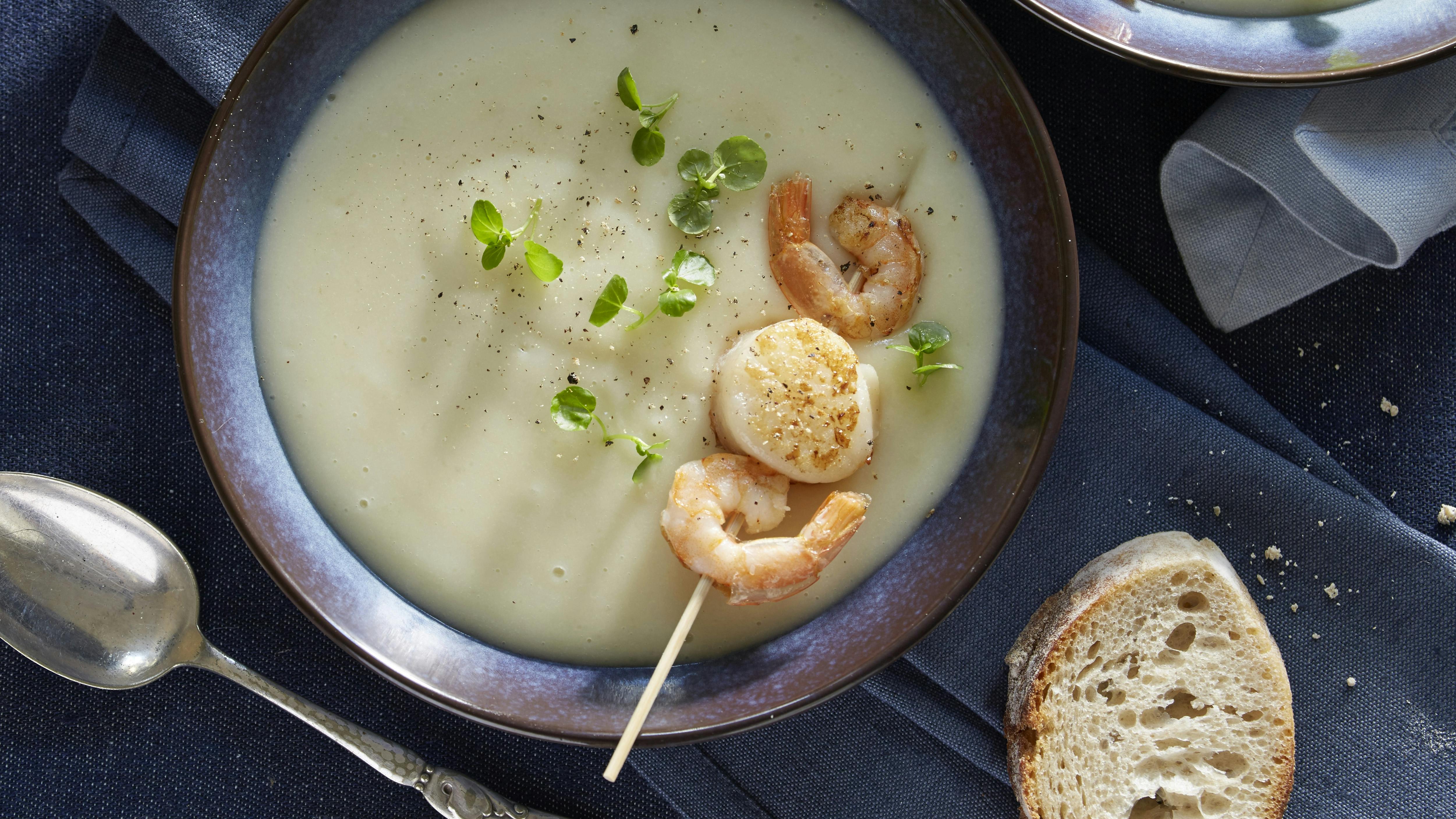 Cremet jordskoksuppe serveret med spyd med kæmperejer og små kammuslinger. Suppen er pyntet med brøndkarse.