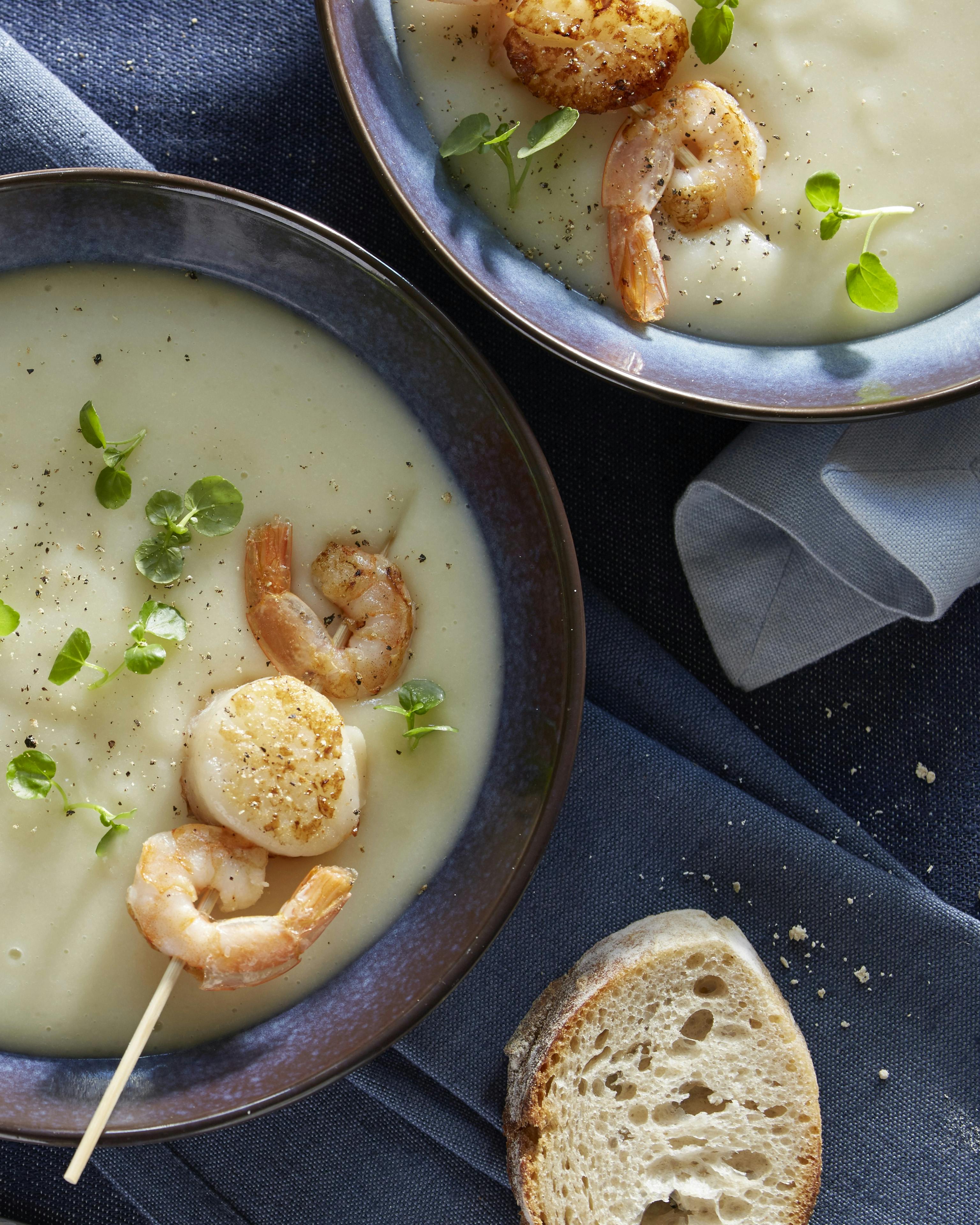 Cremet jordskoksuppe serveret med spyd med kæmperejer og små kammuslinger. Suppen er pyntet med brøndkarse.