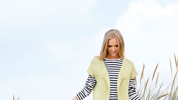 Dame står med kort strikket trøje på stranden