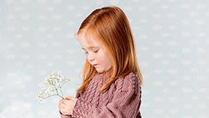 Strikket pigekjole: Lille pige i lyserød strikket kjole står med blomst 