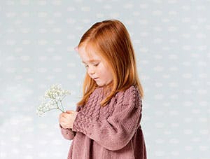 Strikket pigekjole: Lille pige i lyserød strikket kjole står med blomst 