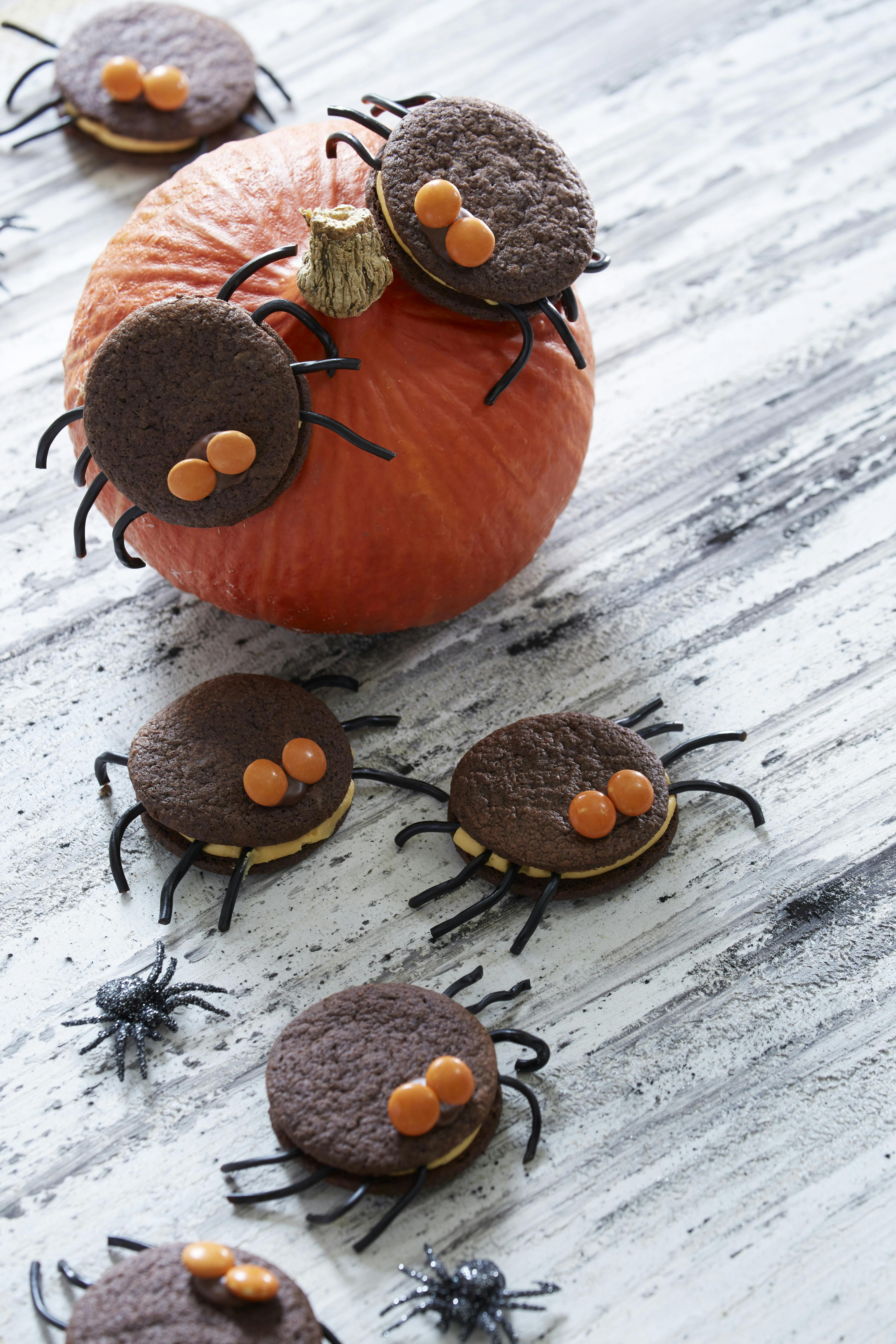 De søde halloweenkager er lavet af kakaokager lagt sammen med hybencreme. de har ben af lakridssnøre og øjne af M&M's