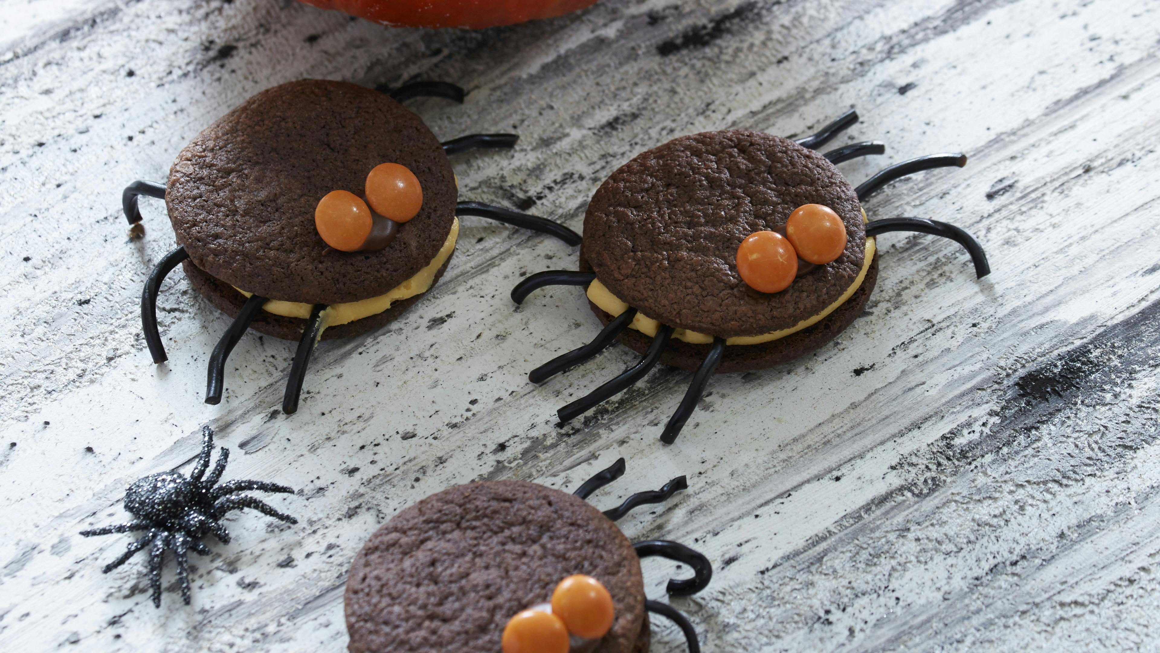 De søde halloweenkager er lavet af kakaokager lagt sammen med hybencreme. de har ben af lakridssnøre og øjne af M&M's