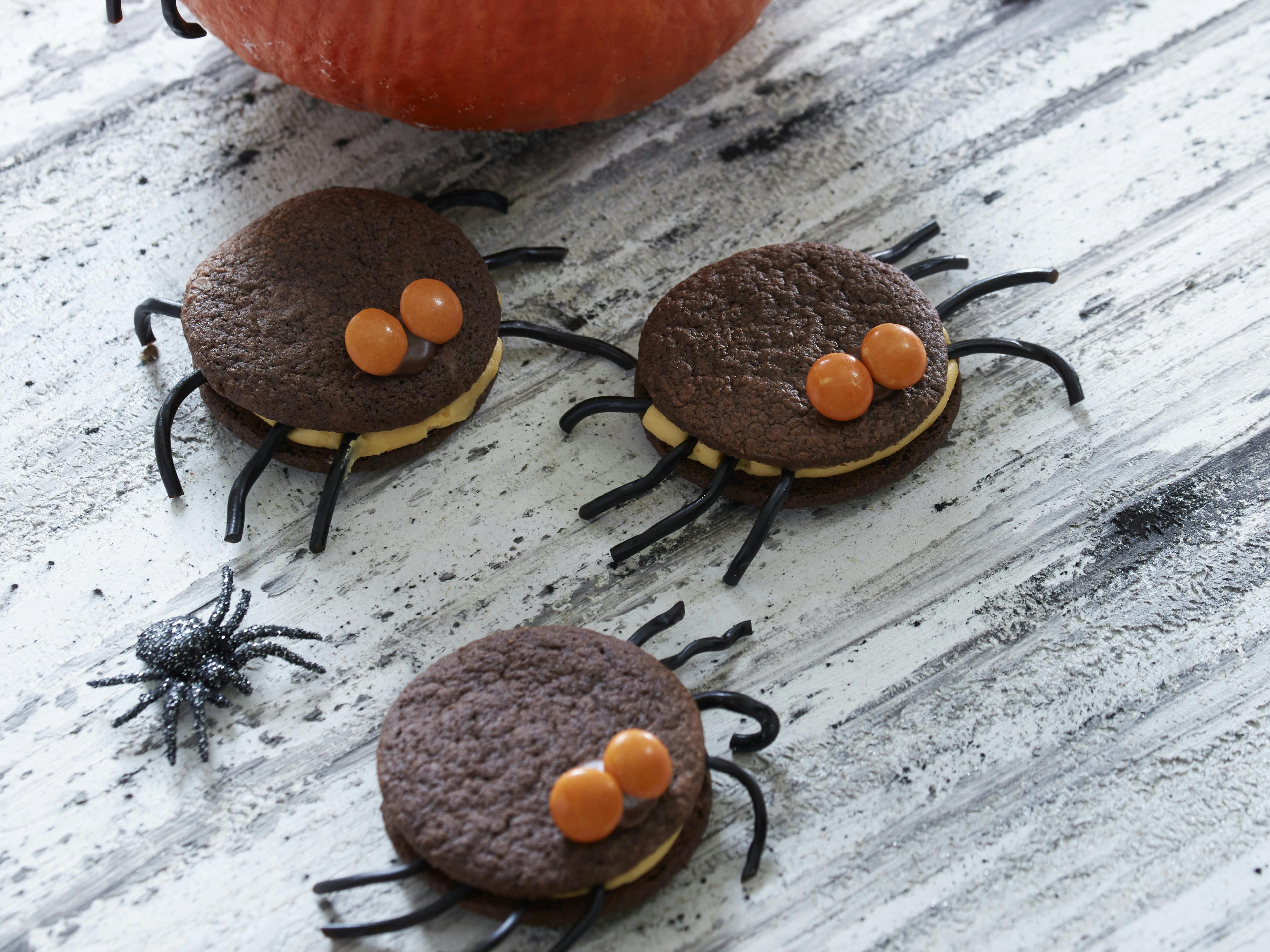 De søde halloweenkager er lavet af kakaokager lagt sammen med hybencreme. de har ben af lakridssnøre og øjne af M&M's