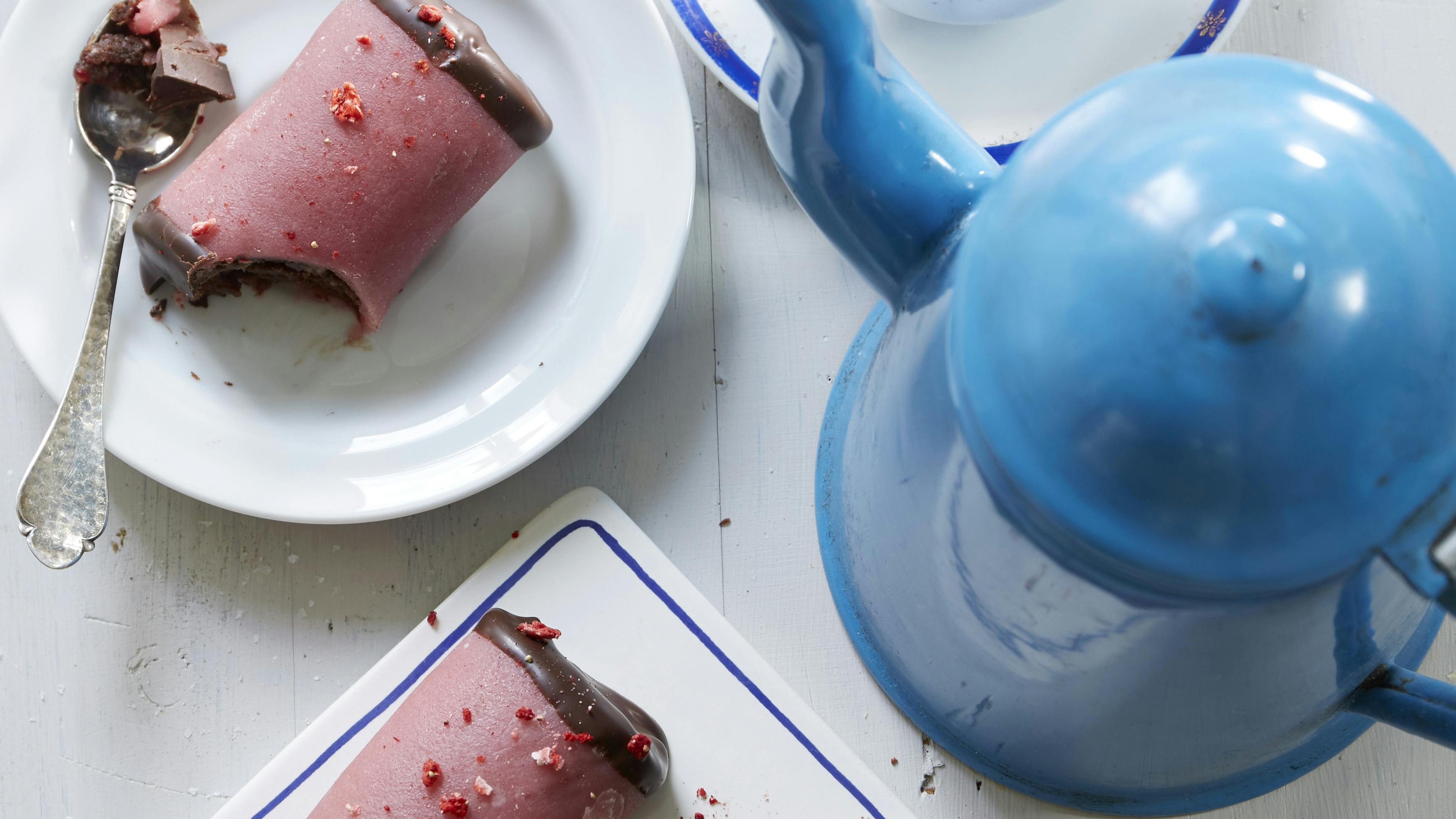 Træstammer af kagemasse med kakao pakket ind i lyserød jordbærmarcipan. Enderne er dyppet i smeltet chokolade