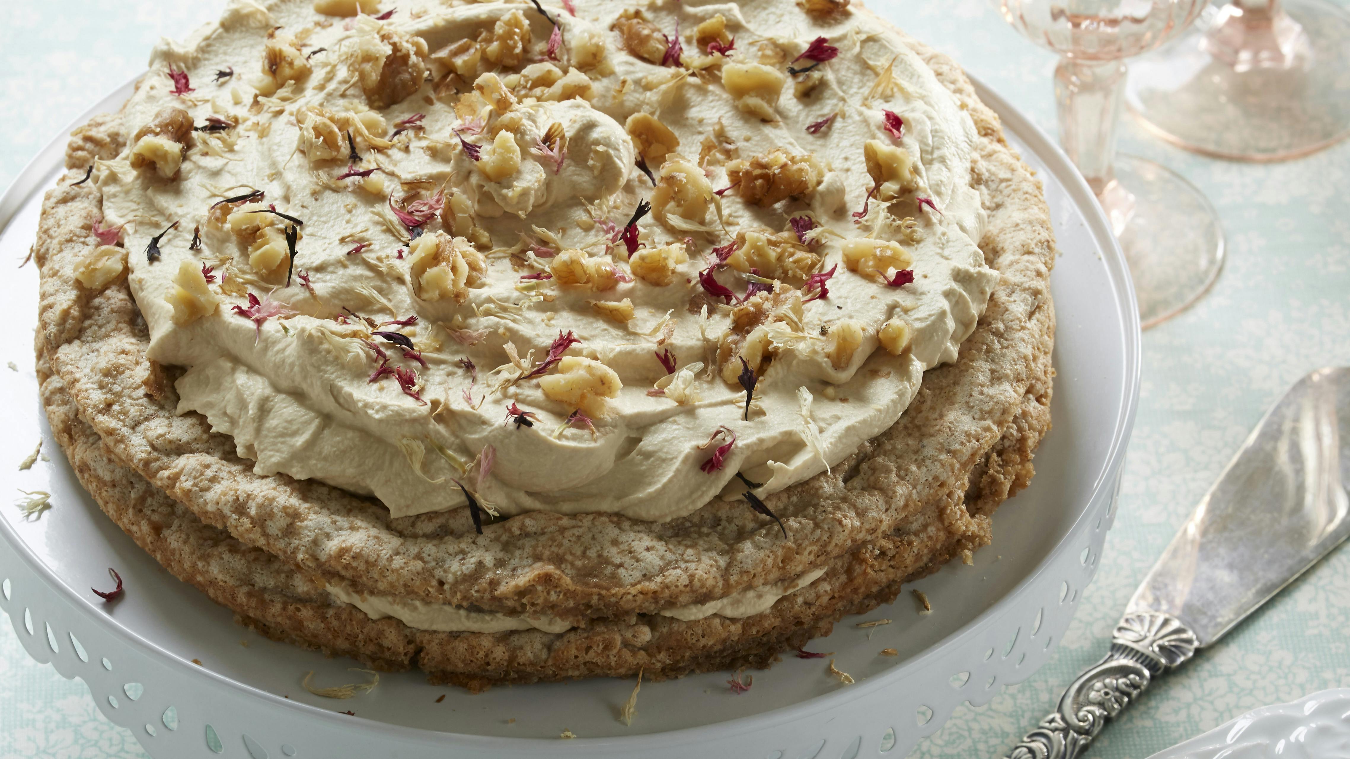 Valnøddekage lavet af to marengsbunde med et lag mokkaflødeskum imellem og på toppen og med drys af hakkede valnødder