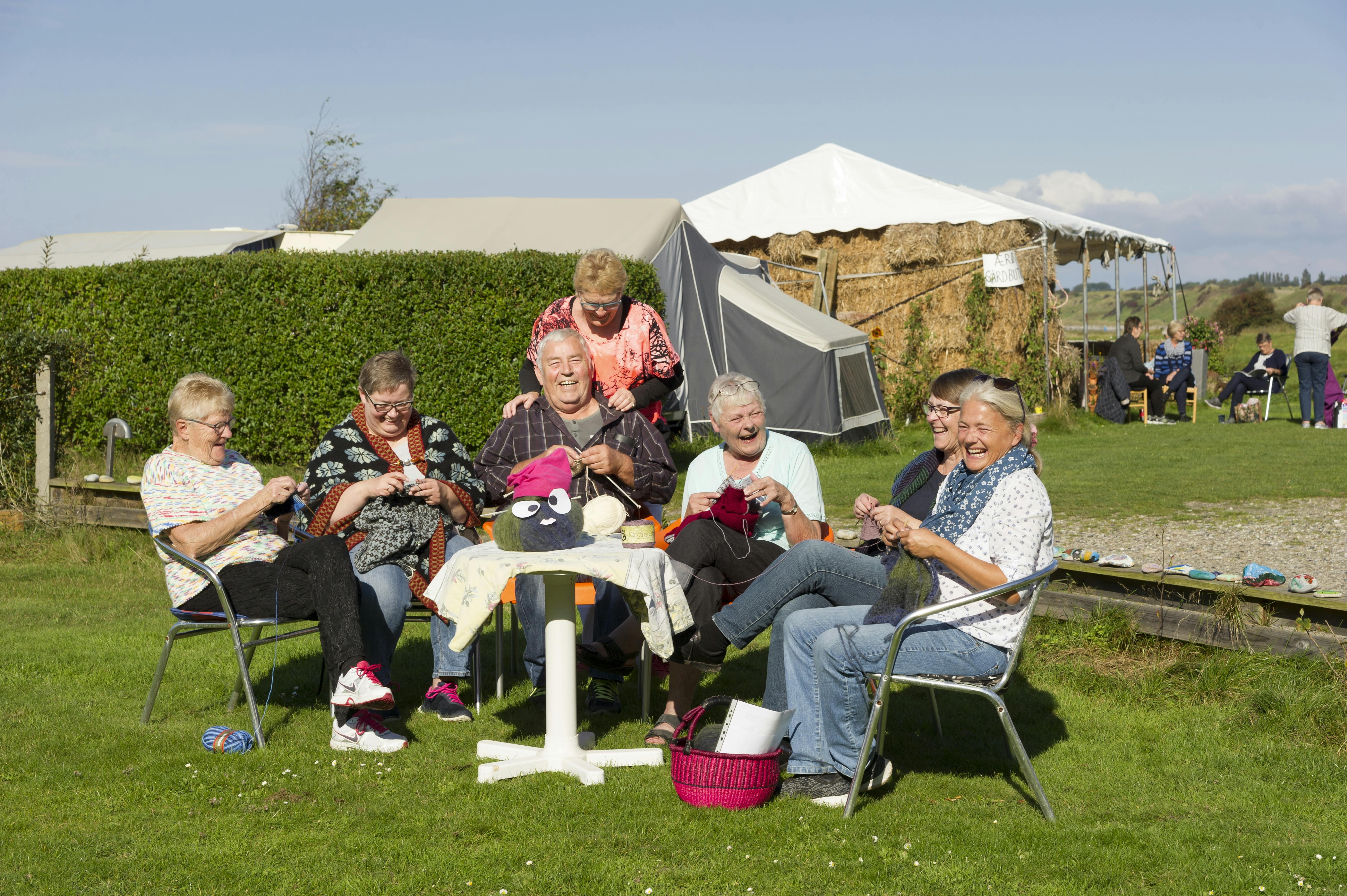 En gruppe mennesker sidder på en campingplads for at strikke sammen