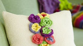 Strikket pude med hæklet blomsterbort i smukke farver