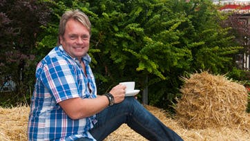 Foto: Jacob Ljørring Vi fik lokket ?Kandis-Johnny? med en tur i høet, da han skulle fotograferes med en kop kaffe. I det travle turnéprogram indgår alle mulige slags former for kaffe. ? 60 kopper om dagen, overdriver han grinende